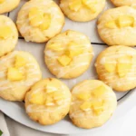 A plate of freshly baked pineapple cookies with pineapple slices and mint leaves on a white serving platter.